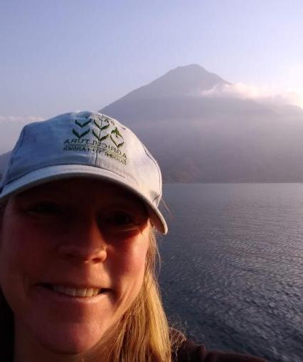 A person smiling in front of water and a mountain